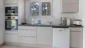 A modern kitchen with white cabinetry, a Bosch dishwasher, a built-in oven, a microwave, and a window with a view of trees. - 100m from sea, house 6 adults & 4 kids (Mesquer)