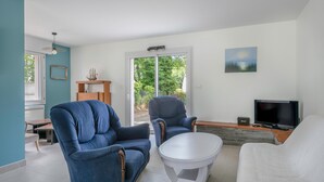 A modern living room with a TV, two blue armchairs, a white armchair, and a small table. - 100m from sea, house 6 adults & 4 kids (Mesquer)
