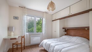 A bedroom with a wooden bed, a desk with a chair, a window with curtains, and a ceiling light fixture. - 100m from sea, house 6 adults & 4 kids (Mesquer)