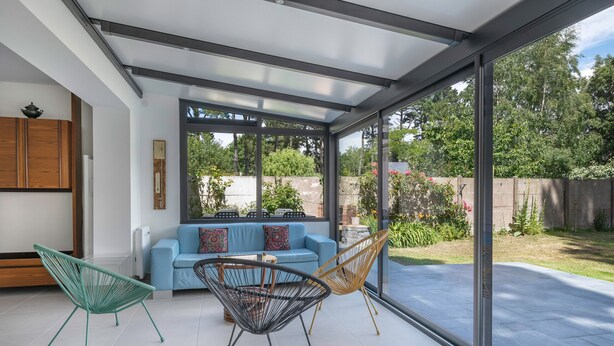 A modern patio with a blue sofa, two chairs, and a glass enclosure. - 100m from sea, house 6 adults & 4 kids (Mesquer)
