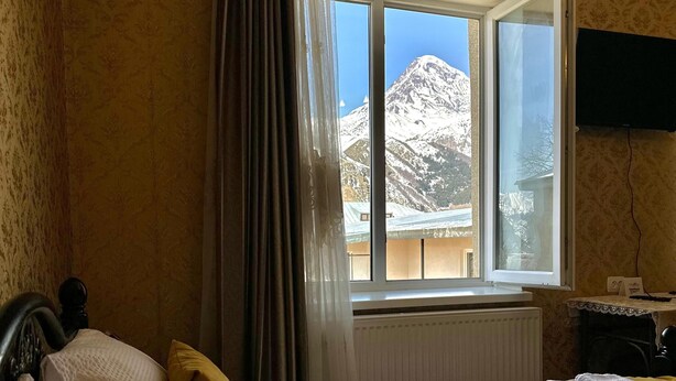 Een hotelkamer met twee bedden, een raam met uitzicht op de bergen, een radiator en een aan de muur bevestigde televisie.