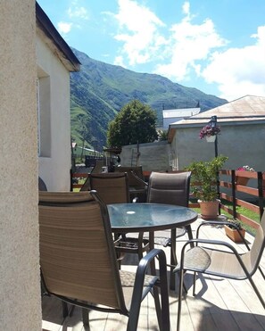 Une terrasse extérieure avec une table et des chaises, un pot de fleurs et une vue sur les montagnes.