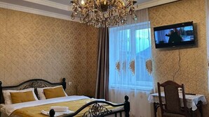 Een slaapkamer met een bed, een kroonluchter, een televisie en een bureau met stoel.
