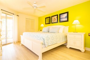 A bright bedroom with a bed, a nightstand, a ceiling fan, and a sliding glass door to the outside.