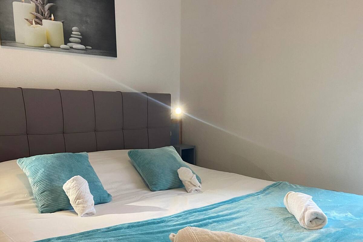 Una cama bien hecha con una colcha y almohadas color turquesa, un cabecero y una obra de arte colgada en la pared.