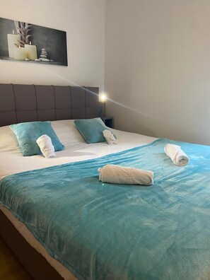 Una cama bien hecha con una colcha y almohadas color turquesa, un cabecero y una obra de arte colgada en la pared.