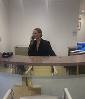 A woman at a reception desk in a hotel lobby with a laptop and a phone.