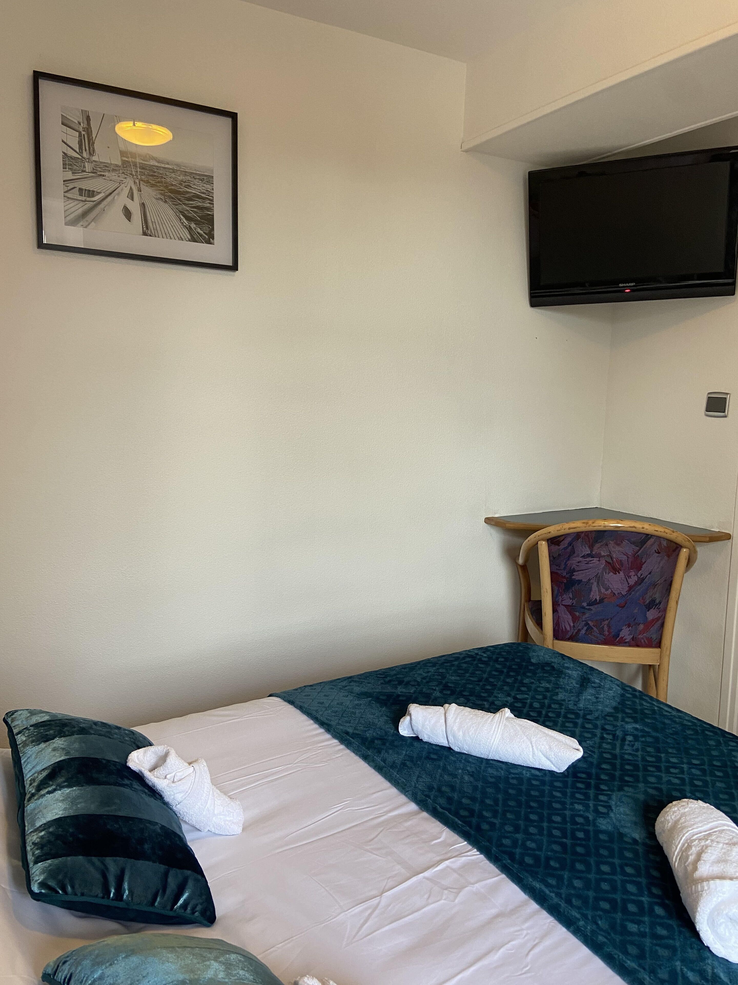 Quarto de hotel com cama, almofadas, uma cadeira, televisão e um quadro na parede.