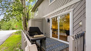 Ein überdachter Außenbereich mit Grill, einem Stoppschild und einer Holzterrasse, die zu einem Haus mit einer Schiebetür führt.
