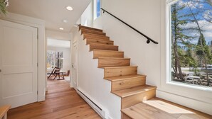 Eine Holztreppe mit schwarzer Handlauf, die zu einem Zimmer mit großem Fenster mit Blick auf eine verschneite Landschaft führt.