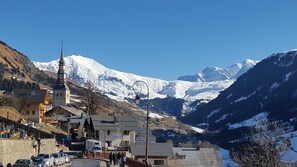 A mountain town with a church, a bell tower, and a snow-covered mountain in the background.