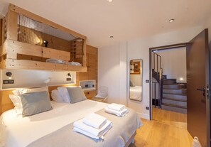 A bedroom with a bunk bed, a large bed with pillows, a mirror, a chair, and a staircase.