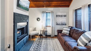 Un salón acogedor con chimenea, un sofá de cuero marrón, un tapete estampado y techo de madera.