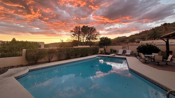 A swimming pool with a view of a sunset and a hilly landscape.