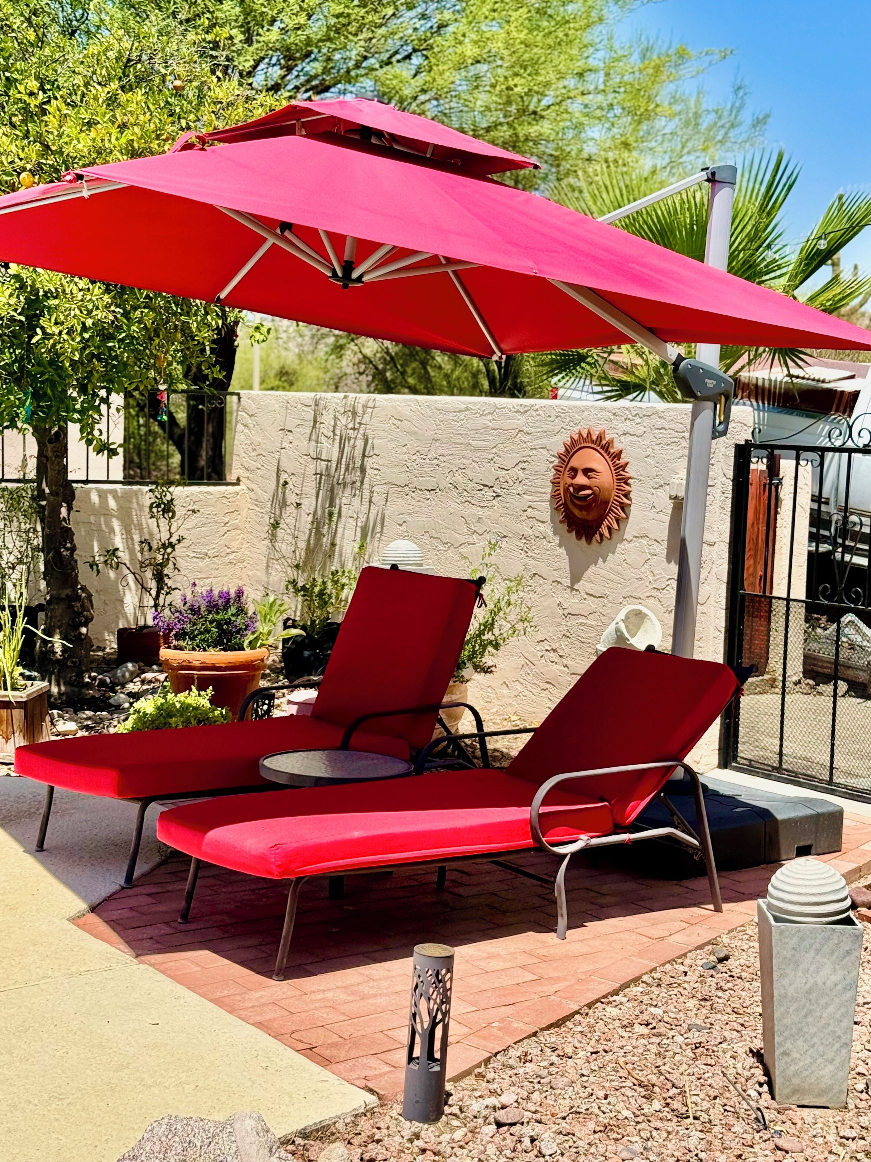 A patio with red lounge chairs and a red umbrella, a decorative wall, and a small garden area.