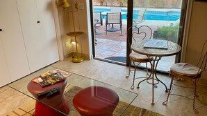 A room with a glass table, red ottoman, and a view of a swimming pool outside.