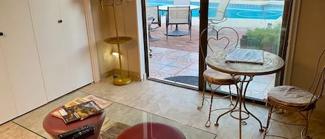 Una habitación con una mesa de vidrio, un reposapiés rojo y vistas a una piscina exterior.