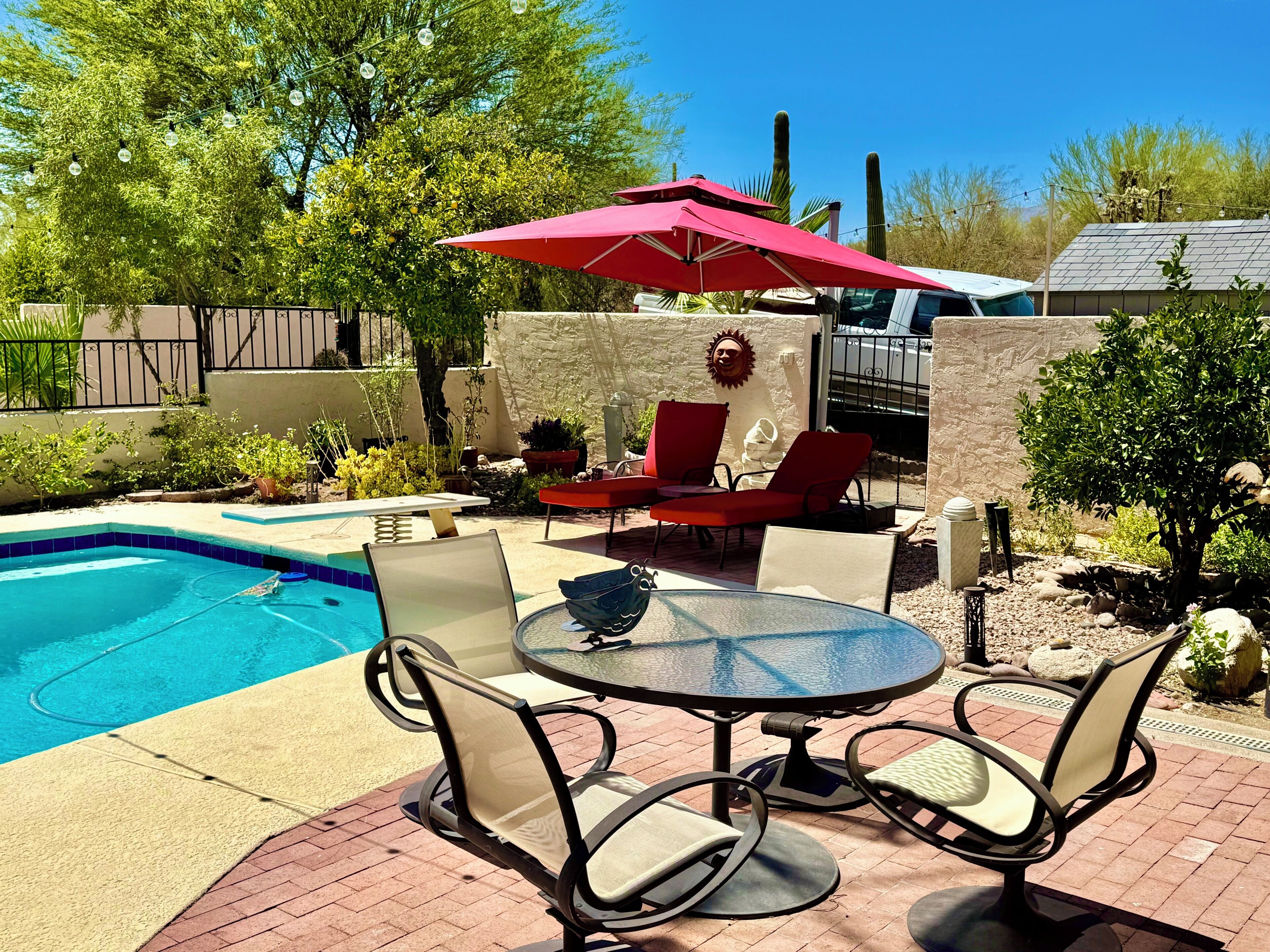Un patio trasero con piscina, muebles de jardín y un paraguas rojo.