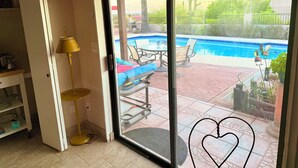 A room with a sliding glass door leading to a backyard with a pool, patio furniture, and a decorative bird sculpture.