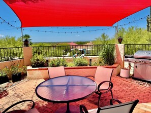 An outdoor patio with a round table and chairs, a barbecue grill, and string lights. - Suite Stay with Heavenly Views (Tucson)