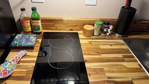 A kitchen with a black induction cooktop, wooden countertop, and various kitchen items including bottles of apple cider vinegar and olive oil.