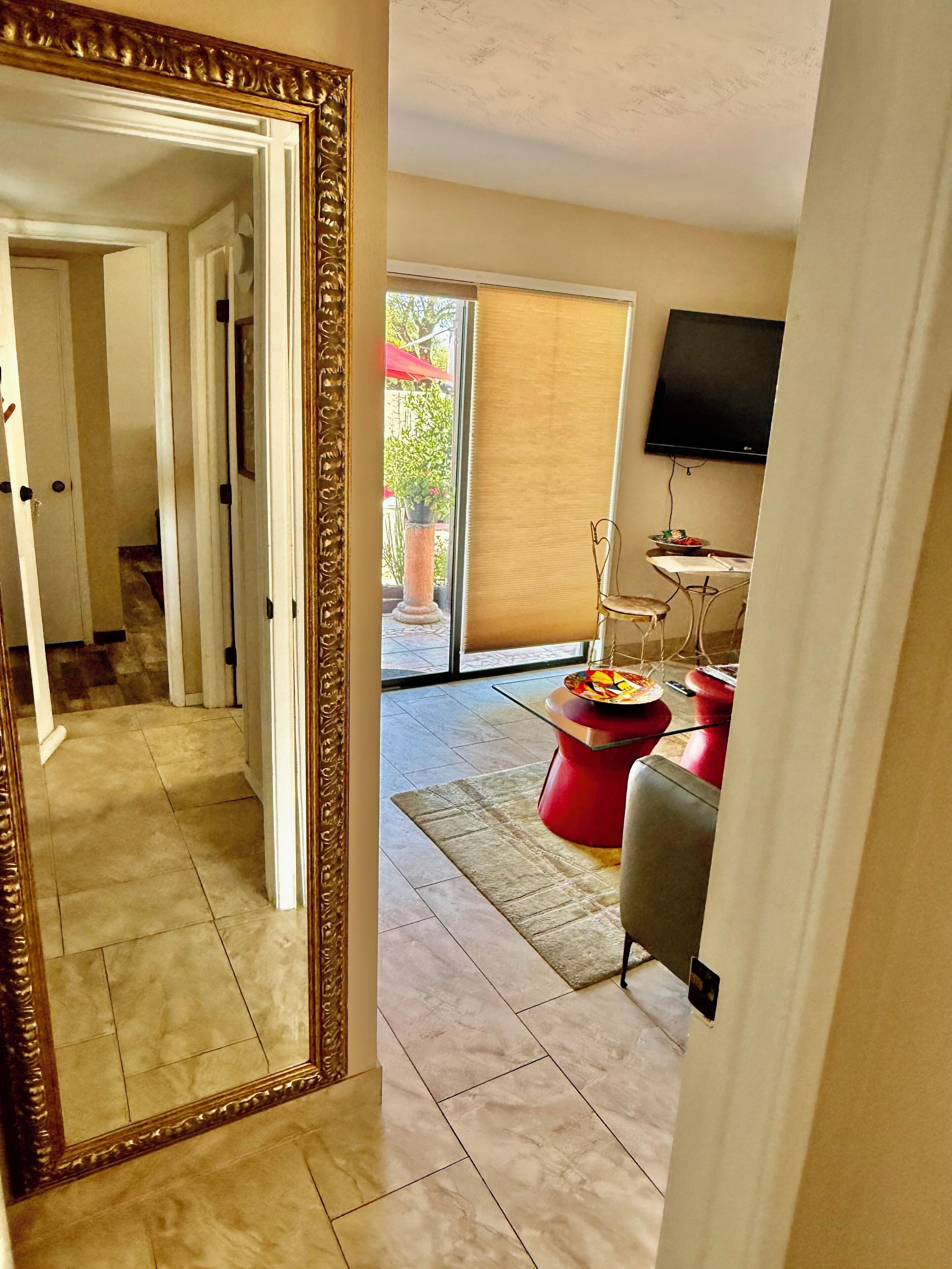 A modern living room with a large mirror, a flat-screen TV, and a dining area with a red table and chairs.