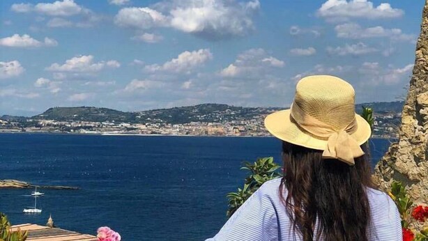 A person overlooking a coastal view with a clear sky, a distant shoreline, and a boat in the water. - Pharus miseni (Bacoli)