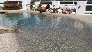 A swimming pool with a pebble-lined edge, surrounded by a white fence and a planter with plants. - Pharus miseni (Bacoli)