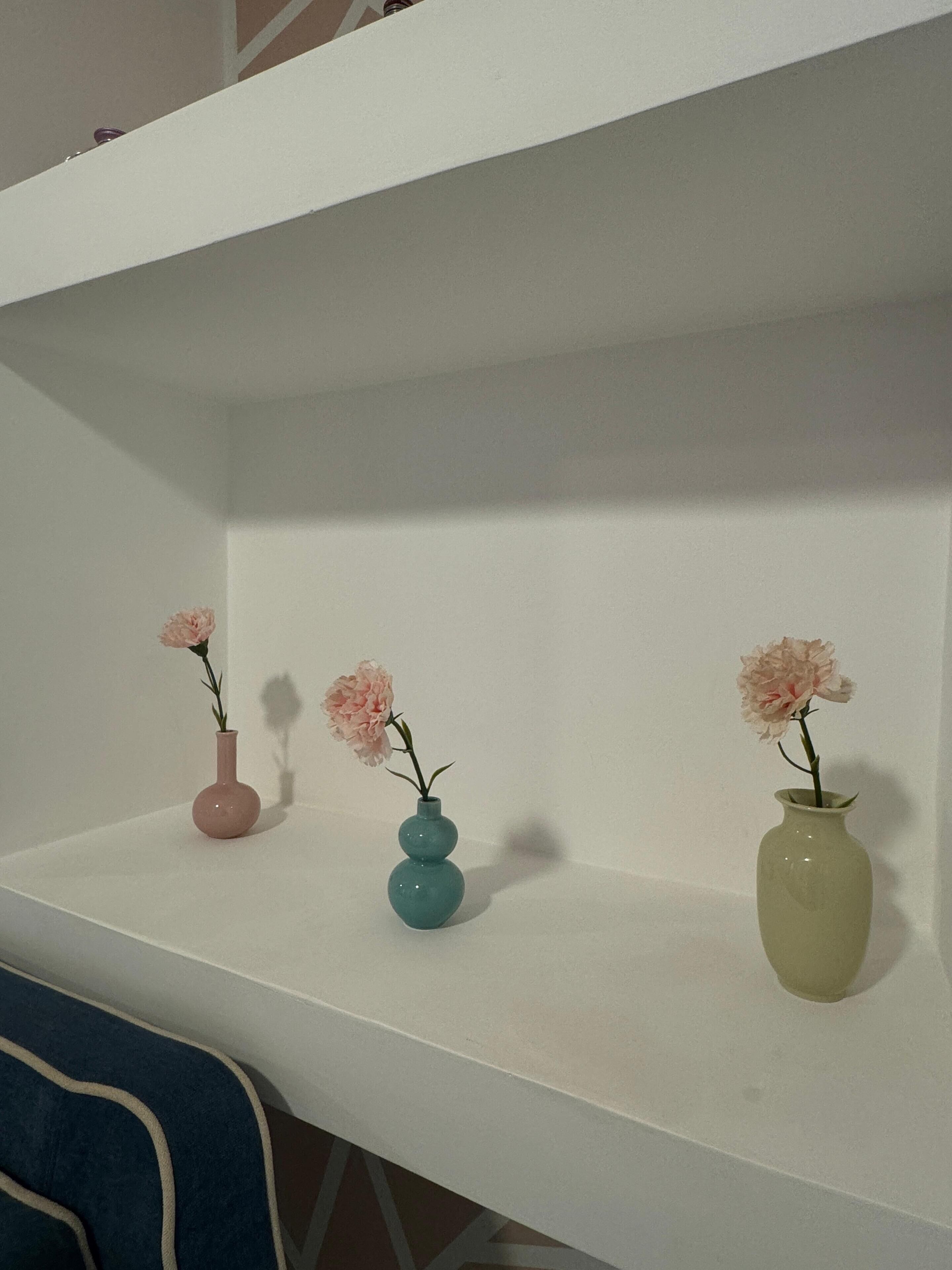 A white shelf with three vases containing pink flowers.