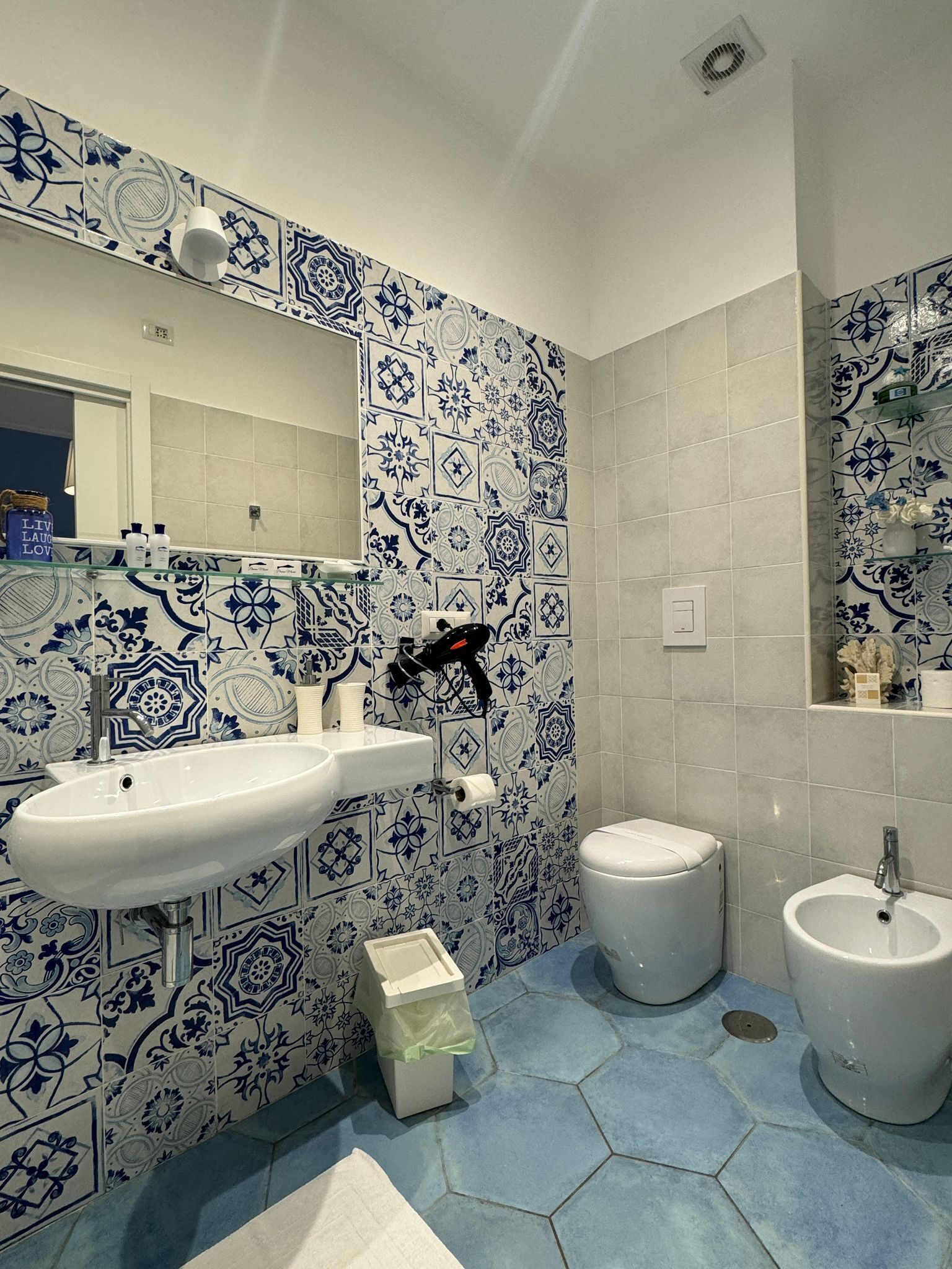 Une salle de bain avec un lavabo blanc, des toilettes et un bidet. Les murs sont recouverts de carreaux aux motifs bleus et blancs.