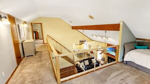 A bedroom with a bunk bed, a desk, and a chair. There is a staircase leading to an upper level.