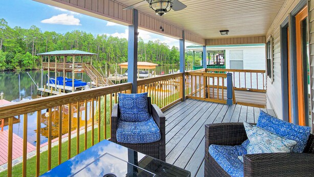A covered deck with wicker furniture and a view of a lake.
