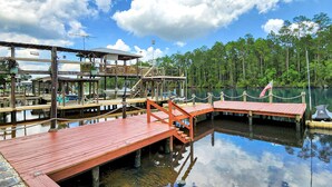 A dock area with wooden walkways, a covered seating area, and a view of a forested lake.