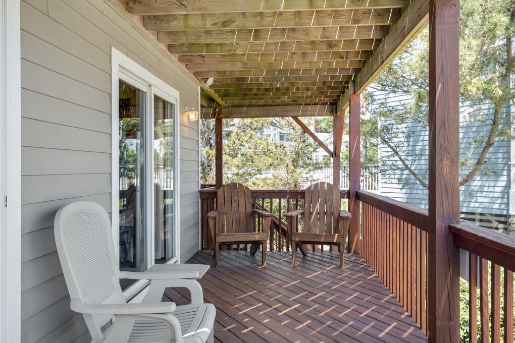 A covered porch with wooden chairs and a table, a wooden deck, and a white door.