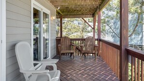 A covered porch with wooden chairs and a table, a wooden deck, and a white door.