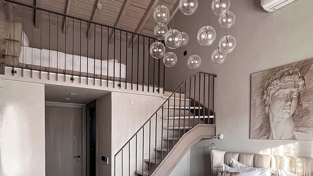 A bedroom with a large bed, a staircase, and a hanging light fixture. - Ala Da Vinci Hotel Alaçatı (Cesme)