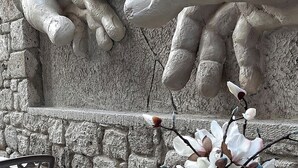 A large stone wall with a relief sculpture of hands reaching out. - Ala Da Vinci Hotel Alaçatı (Cesme)