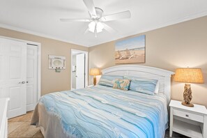 A bedroom with a bed, a ceiling fan, a nightstand with a lamp, and a beach-themed painting on the wall. - FREE Chairs! Gulf Front 1 bed - 2 bath Condo PW510 (PANAMA CITY Beach)