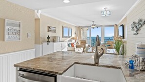 A modern kitchen with a marble countertop, white cabinetry, and a view of the ocean.