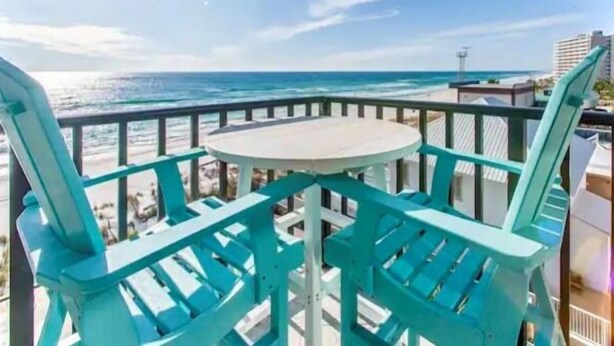 A balcony with turquoise chairs and a round table overlooking the ocean.