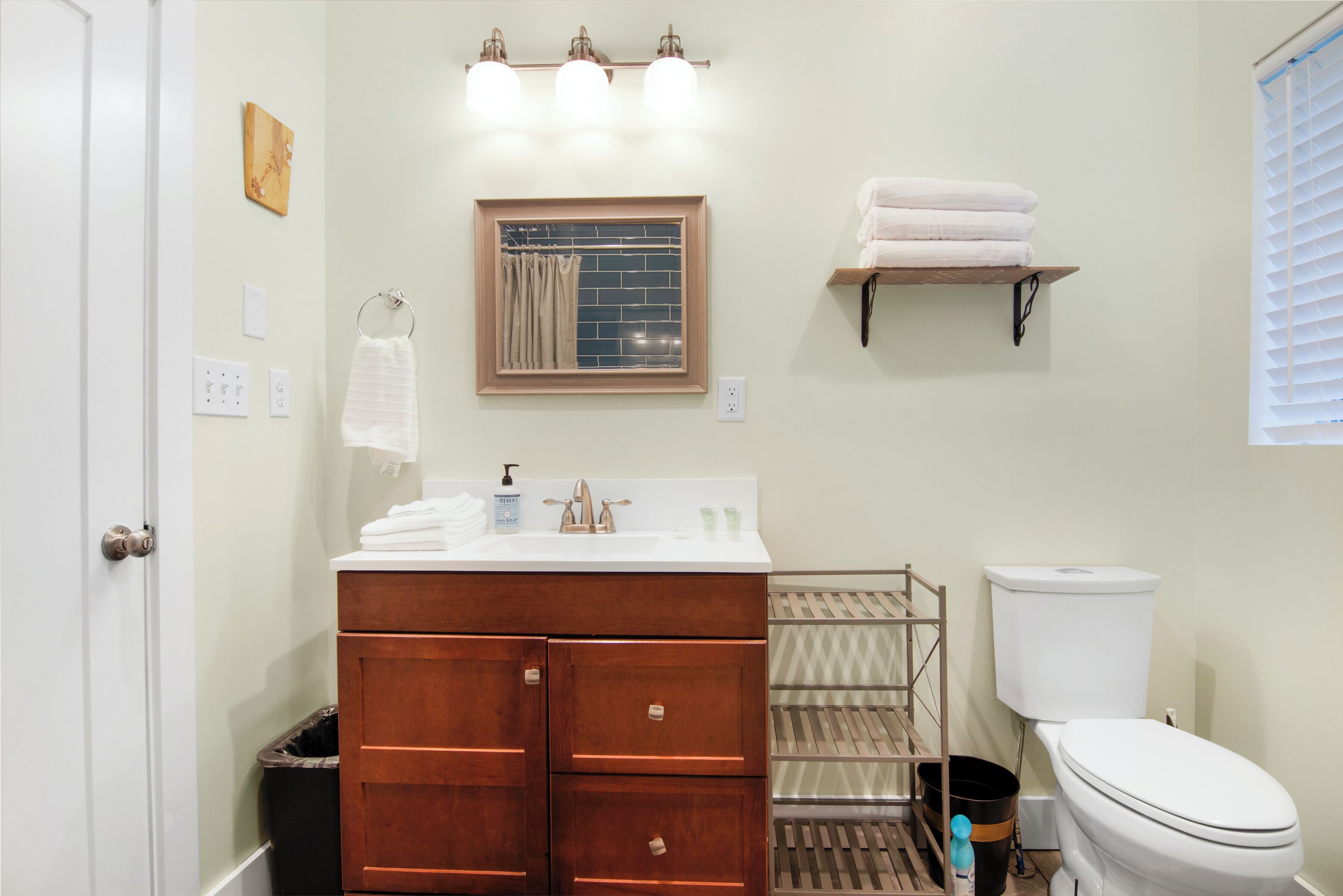A bathroom with a wooden vanity, a toilet, a towel rack, and a shelf with towels.