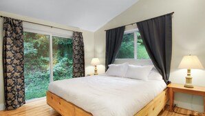 A bedroom with a wooden bed, two bedside tables with lamps, and large windows with curtains. - Secluded modern cabin, short walk to town, river & brewery. <25 min to Asheville (Marshall)