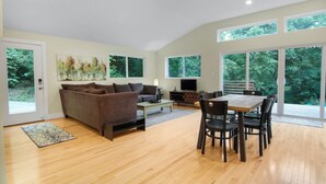 A spacious living room with a sofa, coffee table, and dining area. - Secluded modern cabin, short walk to town, river & brewery. <25 min to Asheville (Marshall)