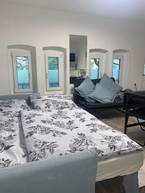 Un dormitorio con cama, escritorio y silla. Hay tres ventanas con vistas a la vegetación.