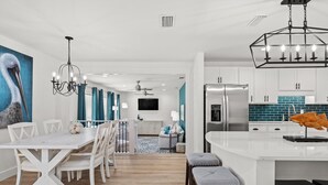 A modern kitchen with white cabinetry, a stainless steel refrigerator, and a large island with stools. - Sleeps 10, Pet Friendly, Fully Fenced Back Yard! (Mexico Beach)