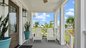 A porch with two white Adirondack chairs, a teal potted plant, and a wooden door. - Sleeps 10, Pet Friendly, Fully Fenced Back Yard! (Mexico Beach)