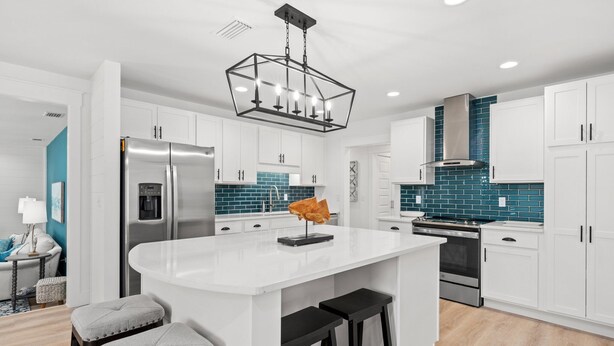A modern kitchen with white cabinetry, a central island with stools, a stainless steel refrigerator, and a blue-tiled backsplash. - Sleeps 10, Pet Friendly, Fully Fenced Back Yard! (Mexico Beach)