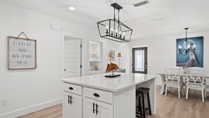 A modern kitchen with white cabinetry, a central island, and a chandelier. - Sleeps 10, Pet Friendly, Fully Fenced Back Yard! (Mexico Beach)