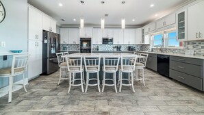A modern kitchen with white cabinets, a central island with bar stools, stainless steel appliances, and pendant lighting. - Your Private Paradise Awaits! (Gulf Shores)