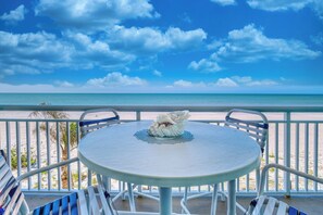 Una mesa redonda con un centro decorativo de concha en un balcón con vistas a la playa.